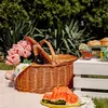 A picnic basket filled with flowers and a bottle of wine, set up on a blanket outdoors with watermelon and drinks on a white crate. Náhled obrázku produktu