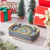 A stack of decorative rectangular plates with a colorful bohemian pattern, arranged on a surface with Christmas decorations like mini pine trees, red gift boxes, and a 'MERRY XMAS' sign in the background. Náhled obrázku produktu
