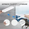 A white automatic telescopic clothesline mounted on a wall, with hands extending and retracting the lines. Insets show close-ups of the product's mechanism and coiled rope. The background features a window with a mountain view. Náhľad obrázku produktu