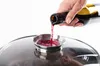 A hand is pouring red wine from a bottle into a small metal dish on top of a glass lid. Produktbild-Vorschau