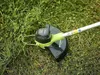 A close-up view of a Greenworks grass trimmer head resting on grass. Náhled obrázku produktu