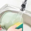 A hand is holding a green funnel under a running faucet in a sink, with a yellow and green sponge nearby. Produktbild-Vorschau