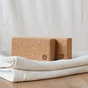 Two cork yoga blocks are placed on top of folded white towels, with a white curtain in the background. Produktbild-Vorschau