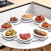A round table with multiple dishes of food arranged on rotating platters, set in a kitchen environment. Anteprima dell’immagine prodotto