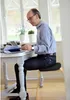 A man is sitting at a desk, working on a laptop, with a window in the background. Voir les images du produit