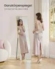 A woman is standing in front of a full-length mirror, looking at her reflection. The mirror has a gold frame and is leaning against a wall. There is a chair and a window in the background. Produktbild-Vorschau