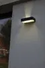 A black outdoor wall light with a white light panel is mounted on a textured gray wall. Produktbild-Vorschau