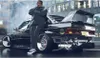 A person leaning against a modified car in an urban setting. Produktbild-Vorschau
