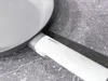 A close-up shot of the handle and edge of a grey and white frying pan, resting on a textured grey surface. Podgląd zdjęcia produktu