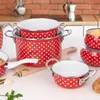A collection of red and white polka dot enamel pots and bowls are arranged on a wooden cutting board and a white surface, with some kitchen elements in the background. Náhled obrázku produktu