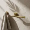 A gold-colored toilet paper holder and a towel rack mounted on a textured wall. Voir les images du produit