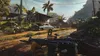 A first-person perspective of a video game scene, showing a weapon in the foreground and a rural village with a car and military vehicles in the background. Podgląd zdjęcia produktu
