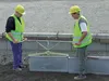 Two construction workers are using a specialized tool to place concrete blocks. Anteprima dell’immagine prodotto