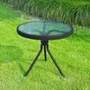 A round glass-topped table with a black metal frame sits on a grassy lawn. Produktbild-Vorschau