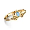 A close-up studio shot of a gold ring with a blue gemstone and small clear stones. Anteprima dell’immagine prodotto
