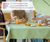 A family is having a meal at a table covered with a light green tablecloth. Produktbild-Vorschau