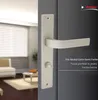 A close-up of a door handle on a dark gray door, with a blurred interior scene visible through an open doorway. Produktbild-Vorschau