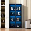 A black glass display cabinet with blue LED lighting, showcasing various decorative items and figures on its shelves. The cabinet is positioned in a room with a light-colored wall and a sofa visible on the right. Produktbild-Vorschau