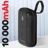 A black power bank with a digital display showing 100% charge, placed on a white surface with a light gray, ribbed background. Podgląd zdjęcia produktu