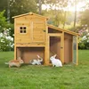 Three rabbits are in front of and inside a wooden rabbit hutch in a grassy yard with flowers in the background. Náhled obrázku produktu
