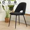 A black dining chair with metal legs is shown in a room with a plant and a window in the background. There are informational icons at the top of the image. Náhled obrázku produktu
