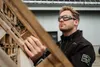 A man wearing safety glasses and a work jacket is inspecting a wooden structure outdoors. Produktbild-Vorschau
