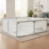 A baby playpen is set up on a rug in a living room, with a sofa and plants in the background. Produktbild-Vorschau