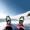 A first-person view of someone sitting in the snow wearing snowshoes, with a snowy mountain and clear blue sky in the background. Voir les images du produit