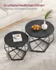 Two round coffee tables of different heights are placed on a textured rug in a living room setting. One table has a book and a cup of coffee, while the other has a bowl of oranges and a white vase with a plant. Podgląd zdjęcia produktu