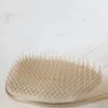 A close-up shot of a hairbrush with beige bristles and a gold trim, resting on a white and light gray textured surface. Anteprima dell’immagine prodotto