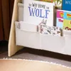 A close-up view of a children's bookshelf with fabric storage pockets holding books and notebooks. Produktbild-Vorschau