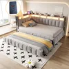 A modern bedroom with a grey upholstered daybed and pull-out trundle, featuring built-in LED lighting and a small inset showing a USB charging port. Náhled obrázku produktu