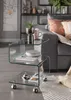 A glass side table with items on it, next to a sofa in a living room. Voir les images du produit