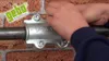 Hands are shown tightening a clamp on a pipe against a brick wall. Náhľad obrázku produktu