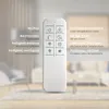 A remote control with its functions labeled in German and English, set against a blurred background of a living room. Produktbild-Vorschau