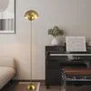 A golden floor lamp stands next to a piano in a living room. Voir les images du produit
