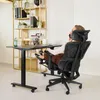 A person is sitting in an ergonomic office chair with their feet up, talking on the phone, next to a standing desk. Produktbild-Vorschau