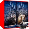 A snowy outdoor scene at night with a house and a tree decorated with icicle-shaped lights. Náhled obrázku produktu