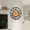 A large wall clock with Roman numerals is mounted on a white brick wall in a living room setting. Produktbild-Vorschau