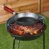 A cast iron skillet is placed on a grill over hot coals, with a wooden fence in the background. Náhľad obrázku produktu