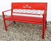 A red metal garden bench with decorative heart accents is shown outdoors on a gravel surface, with a white wall in the background. Produktbild-Vorschau