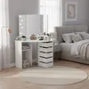 A white vanity table with a lighted mirror is set up in a bedroom next to a bed. Voir les images du produit