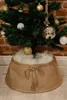 A Christmas tree skirt with a bow in the front, placed around the base of a decorated Christmas tree. Voir les images du produit