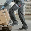 A person wearing work clothes and safety shoes is lifting a box. Podgląd zdjęcia produktu