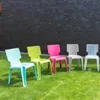 Five colorful plastic chairs are arranged in a row on a grassy lawn in front of a dark brick wall. Produktbild-Vorschau