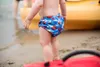 A child wearing a diaper is standing on a beach near a yellow kayak. Produktbild-Vorschau