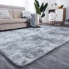 A fluffy gray rug is shown in a living room setting, with a sofa and a cabinet in the background. Produktbild-Vorschau
