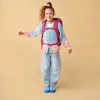 A young girl wearing a backpack and colorful cardigan, jumping with joy. Náhled obrázku produktu