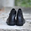 A pair of black Converse Chuck Taylor high-top sneakers are shown from the back, resting on a concrete surface. Produktbild-Vorschau