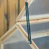 A close-up view of a wooden greenhouse frame with a black metal hinge mechanism. Voir les images du produit